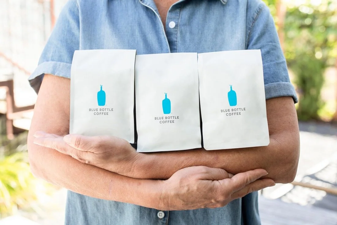 Blue Bottle Coffee white flat-bottom bags held by person — minimalist PET AL PE high-barrier coffee packaging with clean typography design