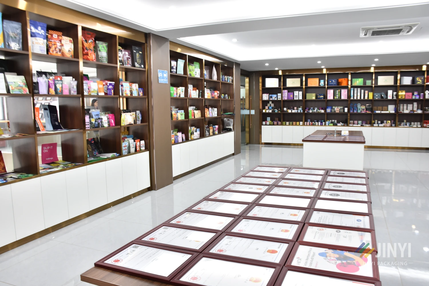 JINYI packaging showroom displaying product samples and certification documents — factory-direct sustainable packaging with verified credentials
