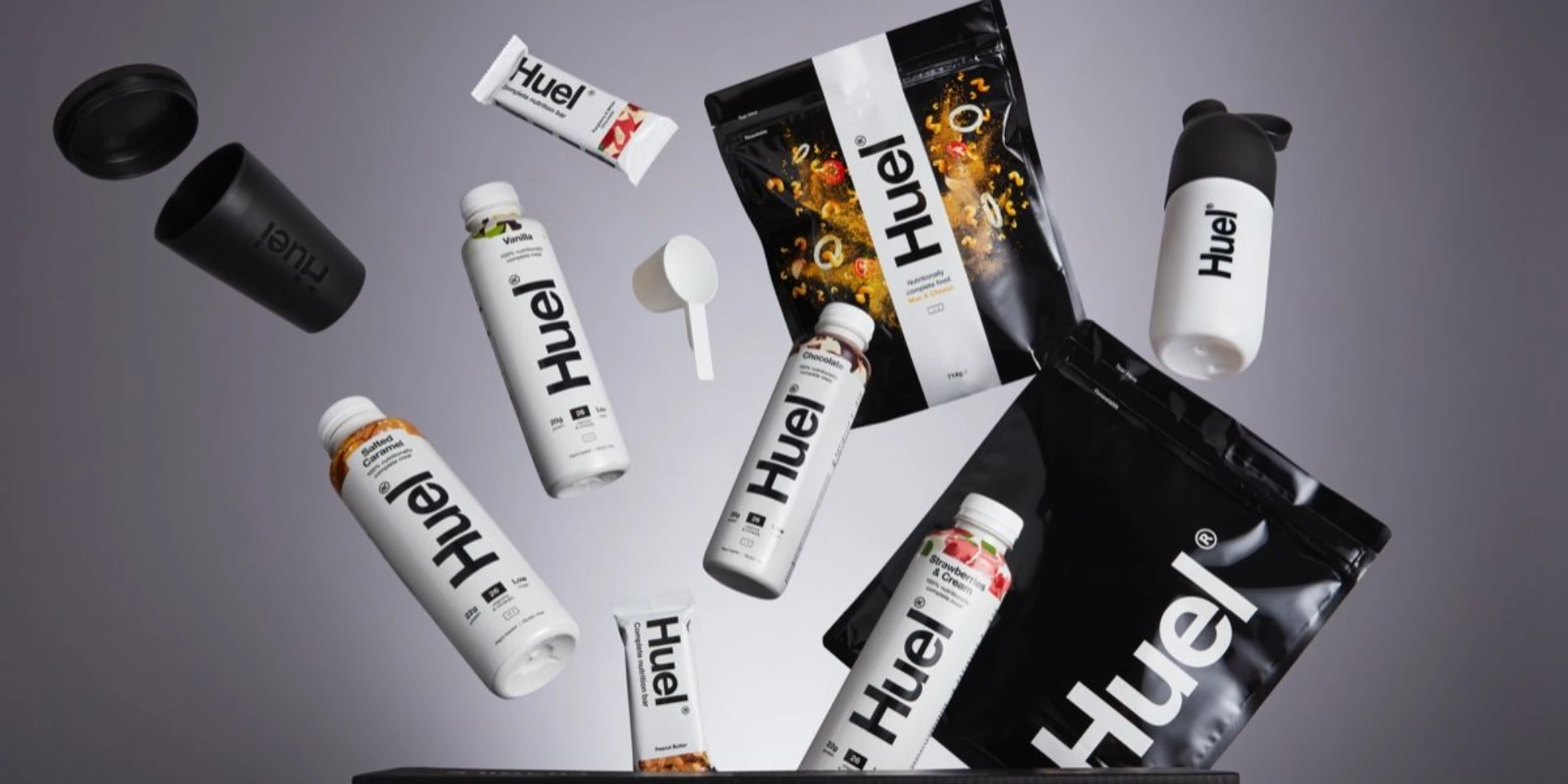 Huel meal replacement product lineup on dark background — stand-up pouches ready-to-drink shakes and bars showing black and white brand packaging design