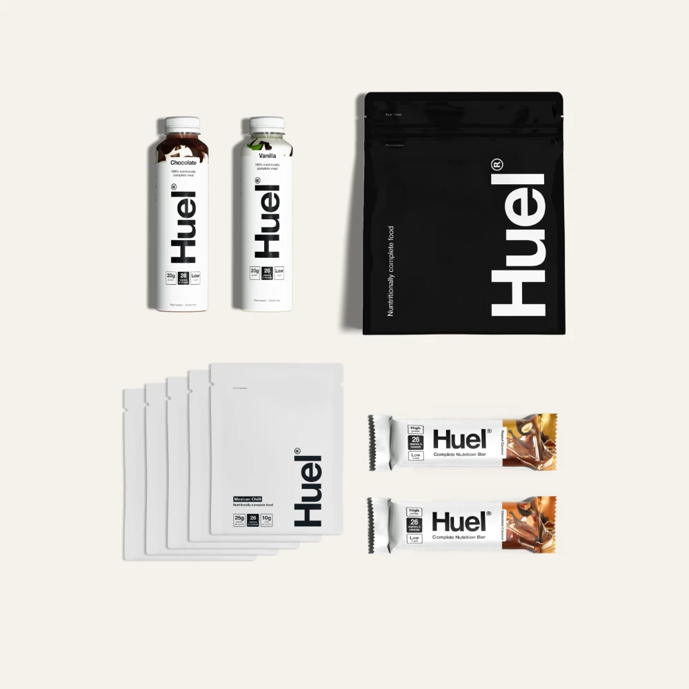Huel complete product range flatlay — black and white stand-up pouches bars and ready-to-drink bottles showing full meal replacement product line packaging