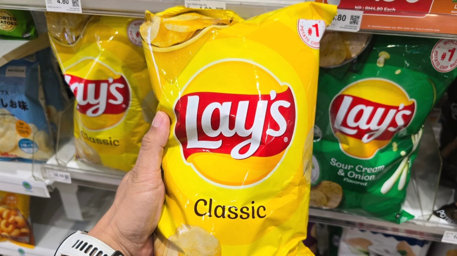 Hand holding a yellow Lay's Classic potato chip bag in a grocery store aisle