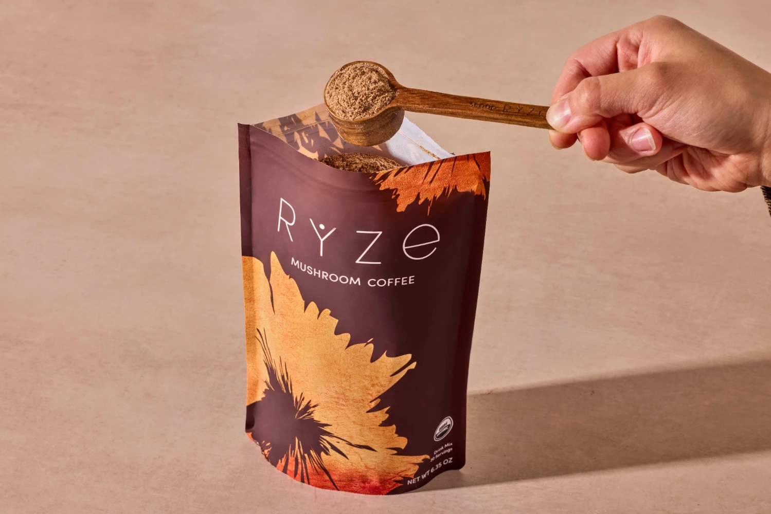 RYZE Mushroom Coffee stand-up pouch com colher de madeira de acácia - embalagem flexível reciclável em tons de terra com desenho de girassol que mostra a experiência de unboxing DTC