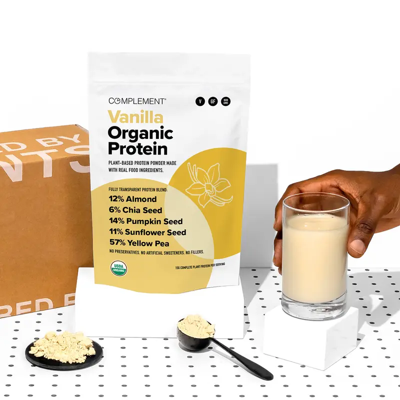 Complement Vanilla Organic Protein powder stand-up pouch held next to a glass of protein shake