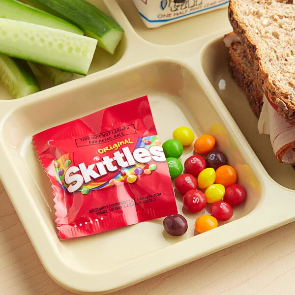 Skittles Original mini bag placed in a lunchbox tray with vegetables and bread