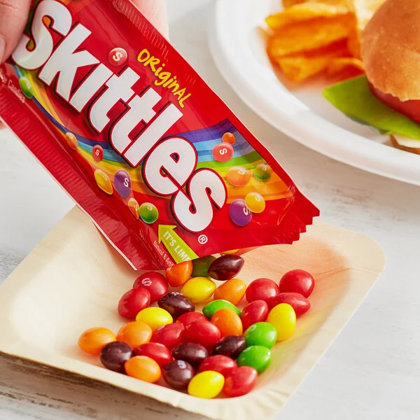 Skittles Original pillow bag with rainbow candies spilling onto a white plate