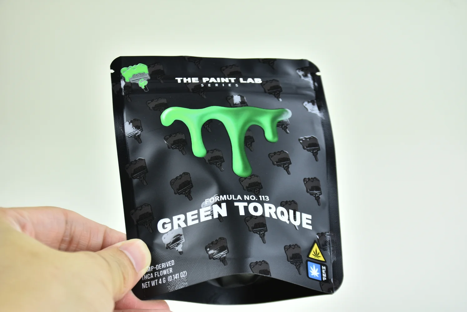 Hand-held The Paint Lab custom pouch — matte black spot UV finish, Green Torque variant, produced by JINYI