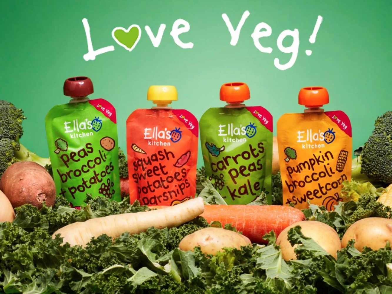 Four Ella’s Kitchen vegetable puree spout pouches displayed with assorted vegetables
